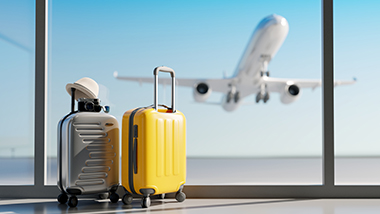 Silver and yellow suitcases on floor of airport. Plane taking off blurred in the background through window.