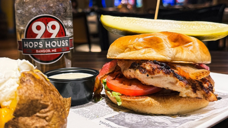 Grilled chicken sandwich with a baked potato side and pickle spear.