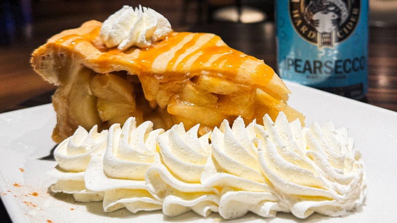 Big piece of golden apple pie on white plate with whipped cream in casino restaurant.
