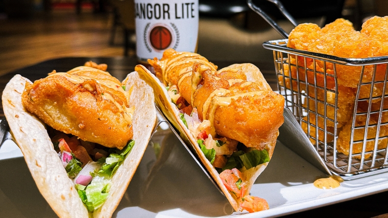 Crispy fried fish tacos in taco holders with a side of tater tots.
