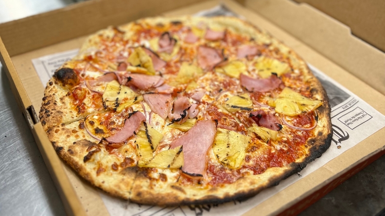 Red sauce pizza with ham and pineapple sliced in a pizza box.