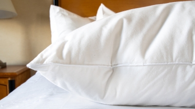 Fluffy white feather pillow on white bed in a hotel room.