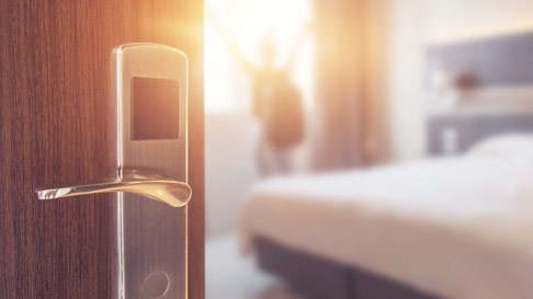 open hotel room door showing bed and someone looking out the window